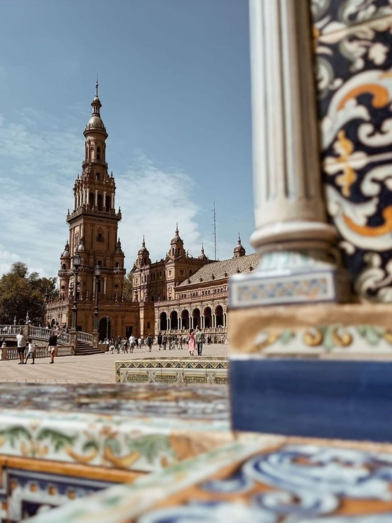 Turismo en Sevilla por la Plaza de España, con la agencia de turismo Turismo Español. Vistas de la Plaza de España en Sevilla, con azulejos ornamentales en primer plano y la torre de España detrás. Foto de Turismo Español.